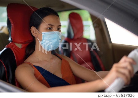 Young Asian woman wearing mask for protection from corona virus outbreak while driving the car Young Asian woman wearing mask for protection from corona virus outbreak while driving the car 65617026