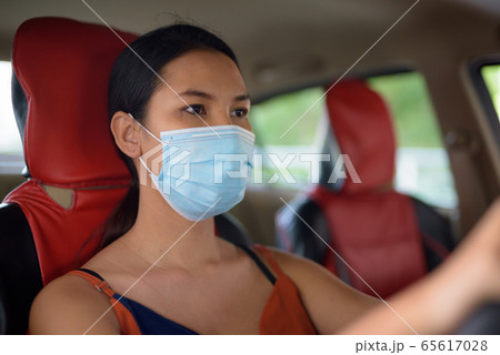 Young Asian woman wearing mask for protection from corona virus outbreak while driving the car Young Asian woman wearing mask for protection from corona virus outbreak while driving the car 65617028