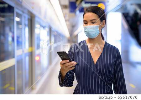 Young Asian businesswoman with mask using phone while waiting at the subway train station Young Asian businesswoman with mask using phone while waiting at the subway train station 65617070