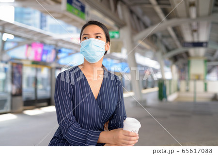 Young Asian businesswoman with mask having coffee on the go while waiting at the skytrain station 65617088