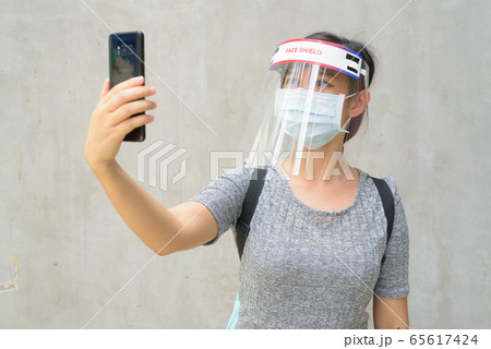 Young Asian woman taking selfie with mask and face shield for protection from corona virus outbreak 65617424