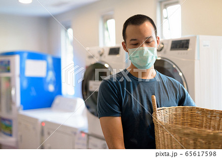 Young Asian man with mask for protection from corona virus outbreak at the laundromat washing Young Asian man with mask for protection from corona virus outbreak at the laundromat washing 65617598