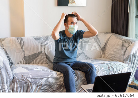 Stressed young Asian man with mask watching tv and looking frustrated at home under quarantine 65617664