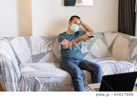 Young Asian man with mask watching tv at home under quarantine 65617666