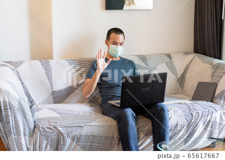 Young Asian man with mask video calling with laptop at home under quarantine 65617667