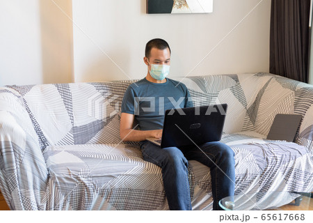 Young Asian man with mask using laptop at home under quarantine 65617668