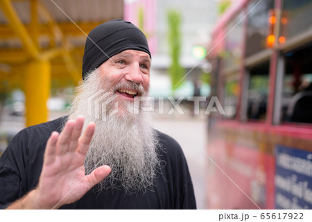 Face of happy mature handsome bearded hipster man waving hand at the bus 65617922