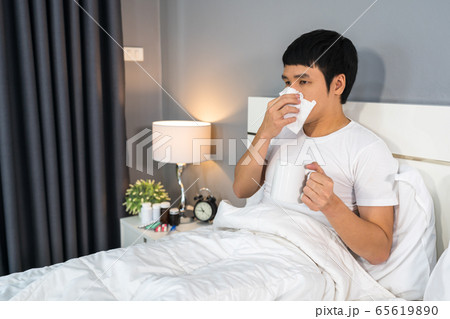 sick man drinking a cup of hot water on bed 65619890