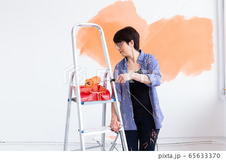 Middle-aged woman painting the walls of new home. Renovation, repair and redecoration concept. 65633370