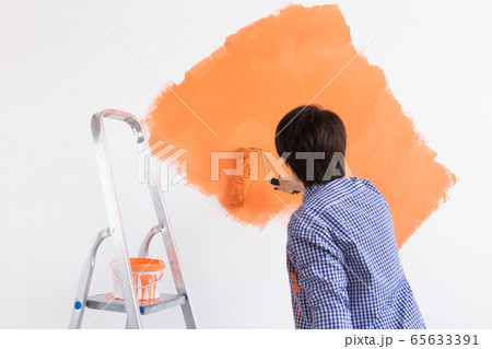 Happy middle-aged woman painting interior wall with paint roller in new house. A woman with roller applying paint on a wall. 65633391