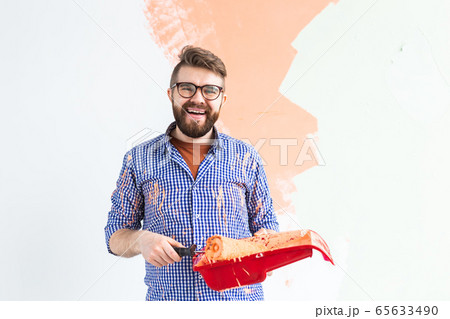 Renovation, redecoration and repair concept - Cheerful guy painting wall in new home. Renovation, redecoration and repair concept - Cheerful guy painting wall in new home. 65633490