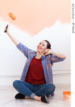 Renovation, redecoration and repair concept - Cheerful woman painting wall in new home. Renovation, redecoration and repair concept - Cheerful woman painting wall in new home. 65634529
