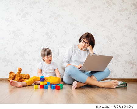 Mom and son sit at home quarantine because of coronavirus COVID19. Mother remote works with laptop, son plays with toy blocks. Self isolation at home. Mom and son sit at home quarantine because of coronavirus COVID19. Mother remote works with laptop, son plays with toy blocks. Self isolation at home. 65635756