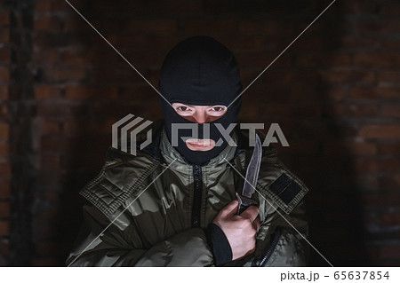 Dangerous criminal in a mask with a knife in the dark against a brick wall Dangerous criminal in a mask with a knife in the dark against a brick wall 65637854