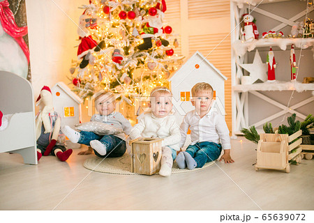 Cute little boys  with blond hair plays with little girl  in a bright room decorated with Christmas garlands near the Christmas tree. Happy childhood. Christmas mood 65639072