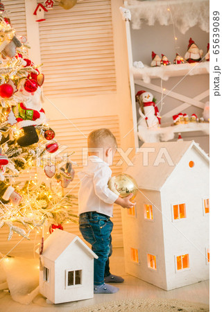 Cute little boy with blond hair plays with toys in a bright room decorated with Christmas garlands near the Christmas tree. Happy childhood. Christmas mood Cute little boy with blond hair plays with toys in a bright room decorated with Christmas garlands near the Christmas tree. Happy childhood. Christmas mood 65639089