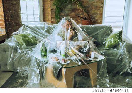 Senior man covered with plastic, eating fast food and drinking beer - environmental pollution by people concept Senior man covered with plastic, eating fast food and drinking beer - environmental pollution by people concept 65640411