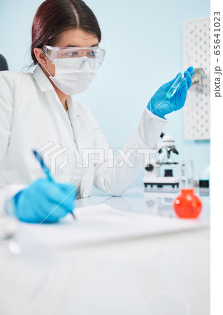 Woman lab technician with test tube in hand makes note. Coronavirus epidemic 65641023