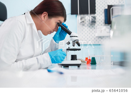 Female epidemiologist looking through microscope in laboratory. 65641056