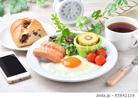 ワンプレート朝食（洋食、目玉焼き、ソーセージ）のイメージ。レーズンパンとコーヒーとスマホと時計。 65642119