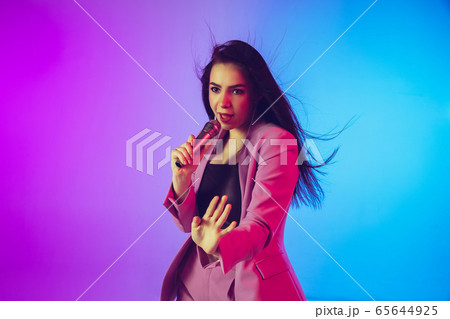 Caucasian female singer portrait isolated on gradient studio background in neon light Caucasian female singer portrait isolated on gradient studio background in neon light 65644925