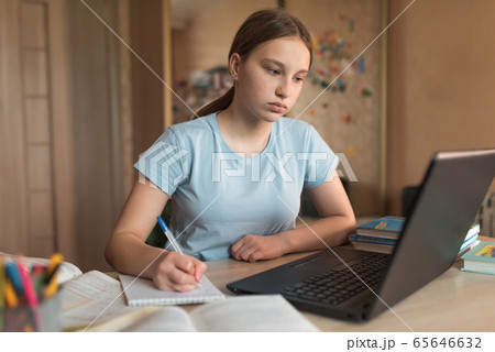Concentrated girl teenager 12-14 years old, home, laptop lessons, notebook writes pen. E-education distance learning Internet and video communications. Accomplishment of lessons and test of exam. 65646632
