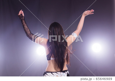 Young woman dancing in Tribal Fusion style. Belly dance on the stage. Back view. 65646989