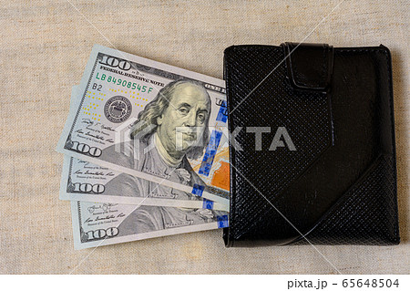 One hundred dollars lie in a black purse on a gray 65648504