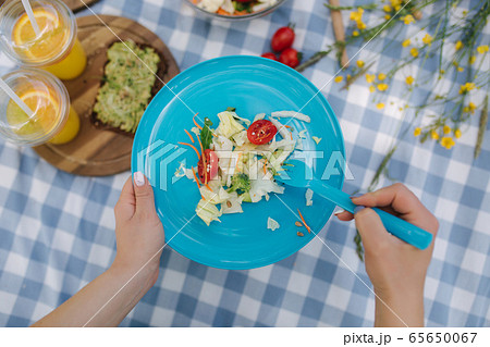 Woman take salad from blue plate on vegan picnic outdoors. Fresh and healthy food 65650067