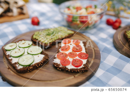 Close-up of Vegan picnic outdoors on blue checkered table cloth. Vegan sandwich with fresh salad and orange juice Close-up of Vegan picnic outdoors on blue checkered table cloth. Vegan sandwich with fresh salad and orange juice 65650074