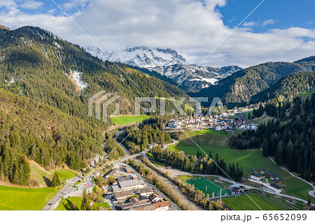 Aerial view of improbable green meadows of Italian Alps, Comano Terme, huge clouds over a valley, roof tops of houses, Dolomites on background, sunshines through clouds 65652099