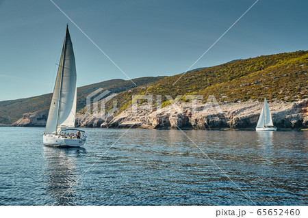 The race of sailboats, a sail regatta, reflection of sails on water, Intense competition, number of boat is on aft boats, Bright colors, island is on background 65652460