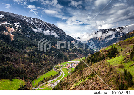 Aerial view of valley with green slopes of the mountains of Italy cloudy weather, Trentino, The trees tumbled down by a wind, huge clouds over a valley, green meadows, Dolomites on background Aerial view of valley with green slopes of the mountains of Italy cloudy weather, Trentino, The trees tumbled down by a wind, huge clouds over a valley, green meadows, Dolomites on background 65652591