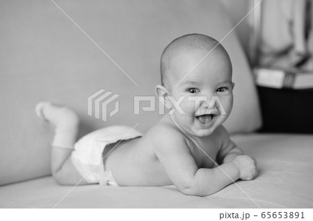 Black and white portrait of little smiling newborn baby. Cute happy baby lying on stomach and laughing, closeup 65653891