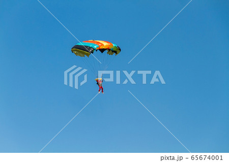 Man soaring in the air currents on a colored parachute against a background of blue. Man soaring in the air currents on a colored parachute against a background of blue. 65674001