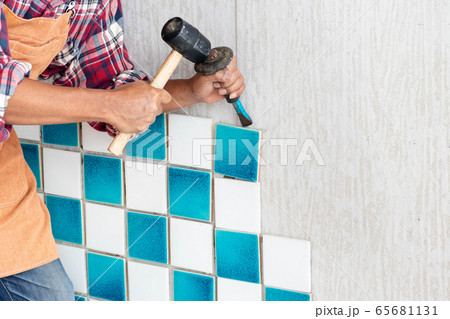 Contract worker using hammer and gouge to chisel or carve the tile from the wall for fixing wall. 65681131