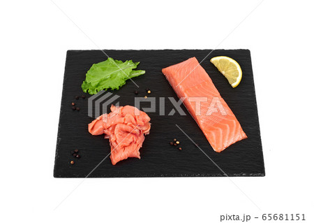 Sliced salmon fillet on the black shale board, with lemon and salad. On white background Sliced salmon fillet on the black shale board, with lemon and salad. On white background 65681151
