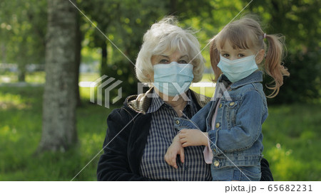 Old grandmother with granddaughter in medical masks in park. Coronavirus Old grandmother with granddaughter in medical masks in park. Coronavirus 65682231