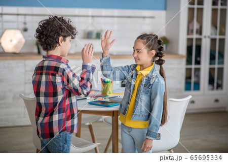 Dark-haired girl and curly boy smiling, giving high five to each other 65695334