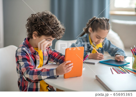 Boy and girl sitting at round table, holding tablets, busy with writing 65695365