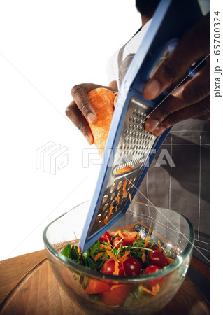 Amazing african-american man preparing unbelievable food with close up action, details and bright emotions, professional cook. Cutting carrot to salad 65700324