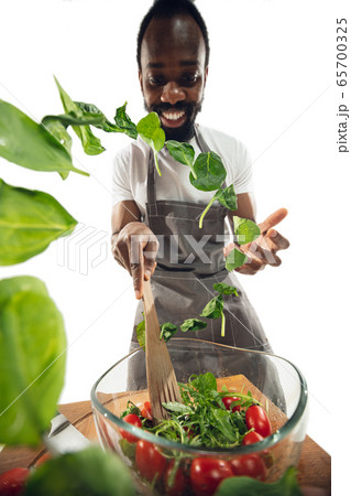 Amazing african-american man preparing unbelievable food with close up action, details and bright emotions, professional cook. Adding salad greens on the fly 65700325
