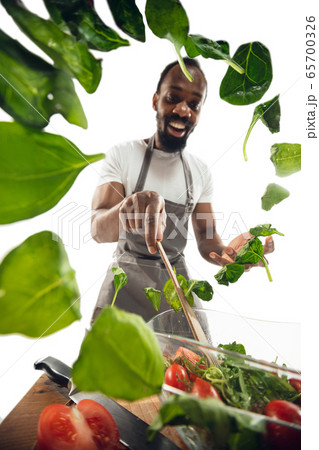 Amazing african-american man preparing unbelievable food with close up action, details and bright emotions, professional cook. Adding salad greens on the fly 65700326