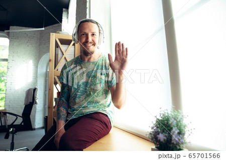 Young man gesturing during a video conference in the living room. Waving, smiling 65701566