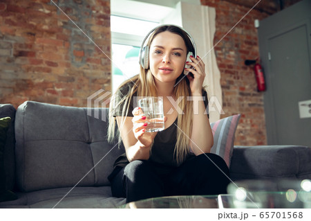 Young woman wearing wireless headphones gesturing during a video conference in the living room. Attented listening Young woman wearing wireless headphones gesturing during a video conference in the living room. Attented listening 65701568