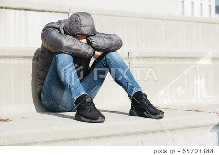 man curled up sitting on an outdoor stairway 65703388