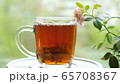 Pouring the tea with leaves of currant, lemon balm, mint, raspberry in a glass cup.Tea party outdoors 65708367