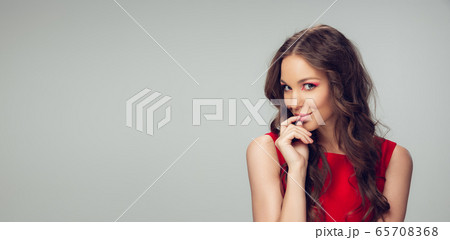 Beautiful young woman with long healthy curly hair and bright make up wearing red dress isolated on grey studio backgroud. Flyer with copyspace. Beautiful young woman with long healthy curly hair and bright make up wearing red dress isolated on grey studio backgroud. Flyer with copyspace. 65708368