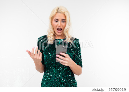 indignant woman in a shiny green dress looks at the phone screen on a white background with copy indignant woman in a shiny green dress looks at the phone screen on a white background with copy 65709019