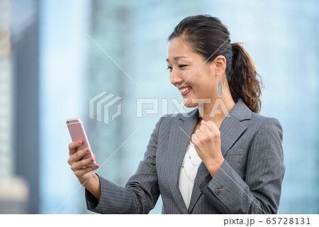 Businesswoman celebrate success while using smartphone outdoors 65728131